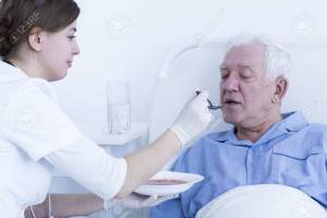 Young nurse feeding the senior patient lying on a hospital bed